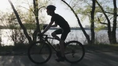 Bisiklet içme suyunda sıska triatlet. Güneş ağaçların arasından parlar. Susuz triathlete eğitim sırasında su içiyor. Triatlon konsepti. Yavaş çekim