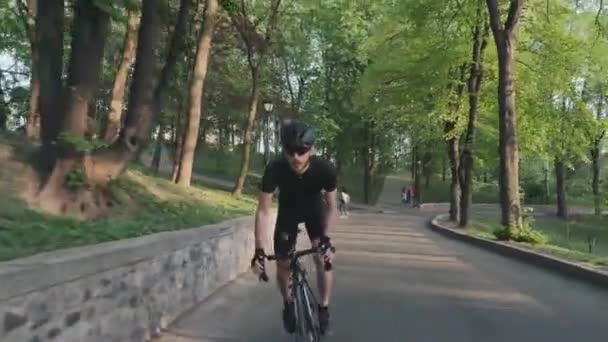 黒いスポーツウェア、メガネ、ヘルメットを着用してサドルの上り坂に乗って焦点を当てた強いフィットサイクリスト。プロのサイクリストのコンセプト. — ストック動画