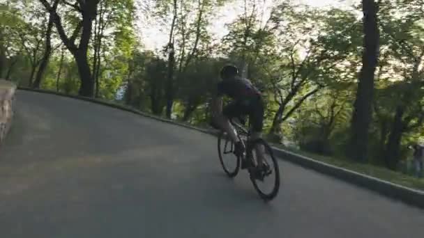 Ein schlanker, athletischer Radfahrer, der mit dem Rennrad im Park absteigt. Radfahrer in schwarzem Outfit auf schwarzem Fahrrad. Radverkehrskonzept. — Stockvideo