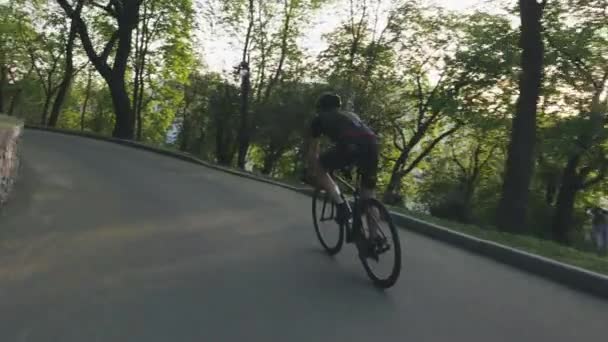 공원에서 로드 바이크를 타고 내려오는 스키니 운동 사이클리스트. 검은 색 의상을 입고 검은 자전거를 타고 자전거. 사이클링 컨셉. 슬로우 모션 — 비디오