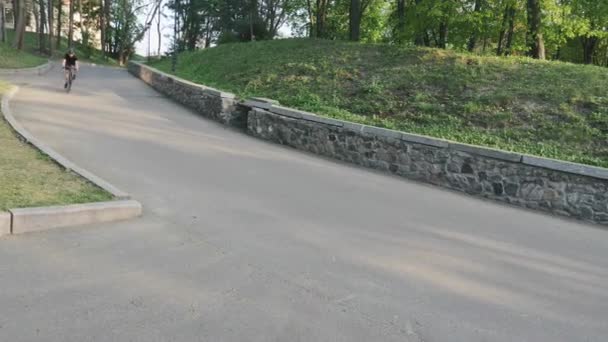 Bisiklet binici hızlı parkta tepeden aşağı iniyor. Kıvrımlı yokuş aşağı yolda kask takan bisikletçi. — Stok video