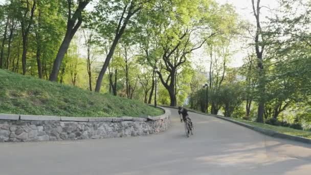 Stark atletisk cyklist tävlar uppåt ur sadeln. Bike Rider stigande kulle bär svarta sportkläder. — Stockvideo