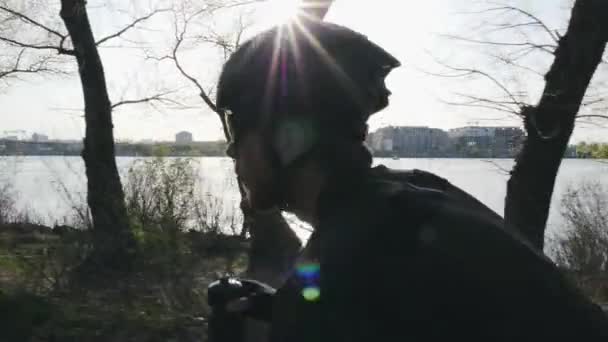Close up view of cyclist with beard drinking water while riding bike. Sun shines through trees reflecting on helmet and sunglasses. — Stock Video