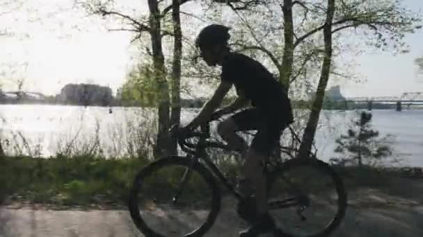 Side follow shot van fietser drinken van waterfles tijdens het rijden door fiets. Dorstige fietser rijden in het stadspark langs de rivier. — Stockvideo