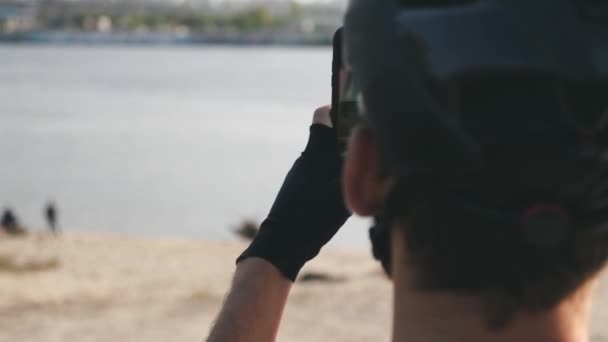 Young cyclist holding phone in his hand taking pictures of river and city wearing helmet, sunglasses and gloves. Slow motion — 비디오