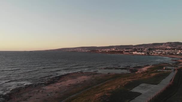 Aerial Drone utsikt över Medelhavet med vågor på solnedgången med stad och berg i bakgrunden. Strand med gångbana. — Stockvideo