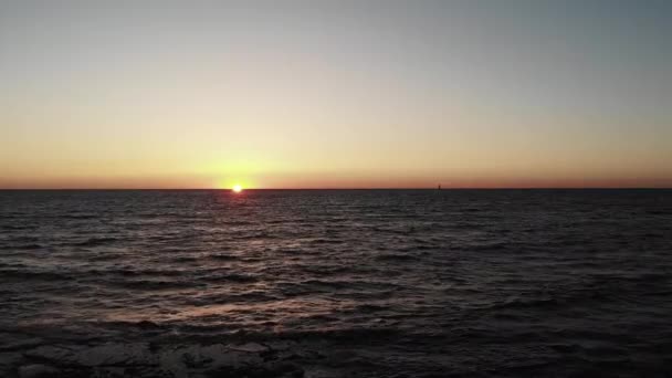 波が地平線上のビーチと小さなヨットを打つ海の上に夕日。波状の海に太陽の道を持つ夕日. — ストック動画