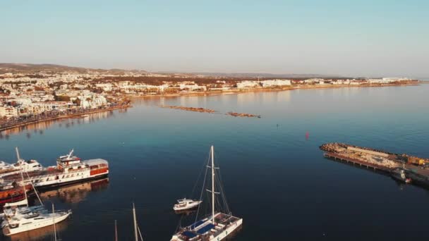 Vzdušný pohled na přístav přístav s člunem plachtění k moři s městem a horami v pozadí. Jachty a motorové čluny plující lodí poblíž mola v přístavu — Stock video