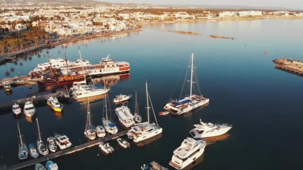 Aerial top view of marina bay with piers and sail ships fisherman boats and motorboats floating. Island city paphos in background — Stock Video