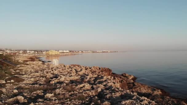 Drohnenaufnahme vom felsigen Klippenstrand mit weißem Denkmal in Paphos Zypern Stadt mit ruhigem See und Burg im Hintergrund. — Stockvideo