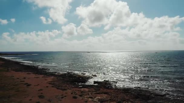 Letecká střela odráží sluneční paprsky na zvlněné moře během západu slunce. Vlny dopadávají na skalnatou pláž. Pobřeží oceánského moře — Stock video