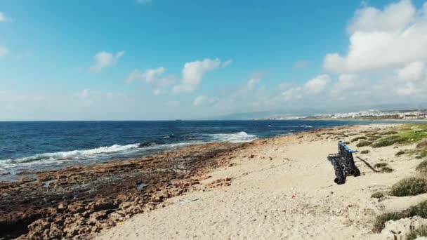 Грязный пляж с пластиковыми бутылками и металлической конструкцией. Вид с воздуха на морские волны, ударяющиеся о скалистый пляж. Штормовое море — стоковое видео