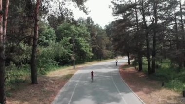 Pembe kıyafet ve siyah kask giyen kadın sevimli bisikletçi onu eğitim rutin bir parçası olarak parkta bir bisiklet sürmek. Bisiklet konsepti. Frontside drone görünümü.