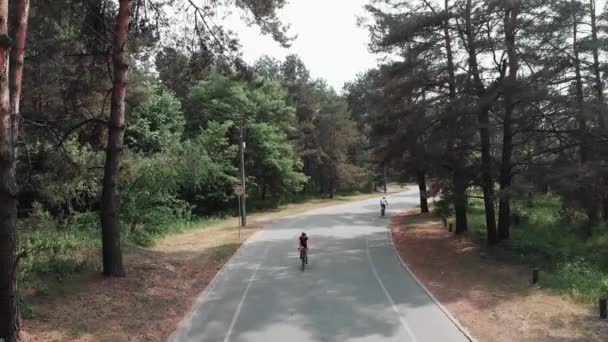 Mujer linda ciclista con traje rosa y casco negro monta una bicicleta en el parque como parte de su rutina de entrenamiento. Concepto de ciclismo. Vista frontal del dron . — Vídeo de stock