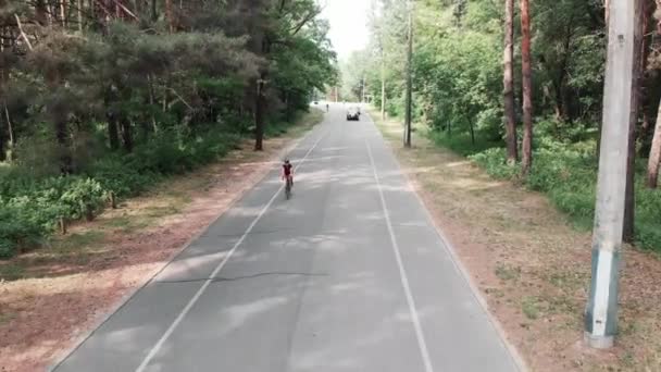Fokuserad ung attraktiv triathlet flicka i en svart hjälm och rosa sportkläder är träning i parken. Frontside följa skott. Triathlon Concept — Stockvideo