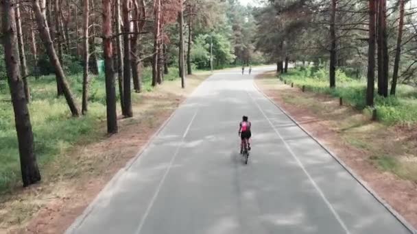 Joven hermosa ciclista en traje rosa monta una bicicleta en el parque. Concepto de ciclismo. Vista trasera del dron . — Vídeos de Stock