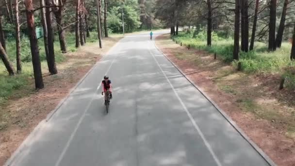 穿着粉色运动衫和黑色头盔的年轻迷人的女运动员正在夏天的森林里享受骑自行车的乐趣。 无人机视图. — 图库视频影像