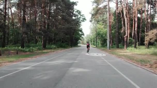 Jovem mulher triatleta atraente está treinando em uma bicicleta na floresta. O traseiro segue o tiro. Vista para drones — Vídeo de Stock