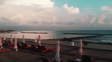 Arka planda deniz ile şezlong ve şemsiye ile plaj alanı üzerinden uçan Drone