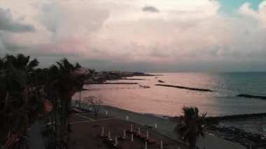 Akşamları boş şezlong ve şemsiyeile nüfussuz turist ve plaj alanı havadan görünümü. Terk edilmiş iskelede yürüyen, gülen ve eğlenen çiftin drone fotoğrafı