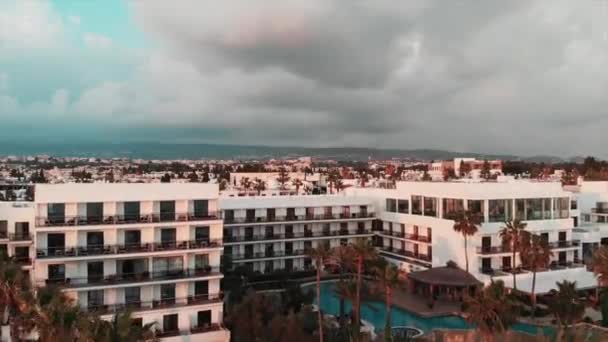 日没時のホテルや建物の航空写真。スイミングプールと手のひらを持つホテルの空中ドローンショット — ストック動画