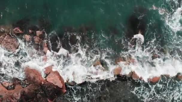 Luchtfoto van sterke golven die rotsen raken en spetteren. Drone-weergave van helder blauw Oceaan water met wit schuim — Stockvideo