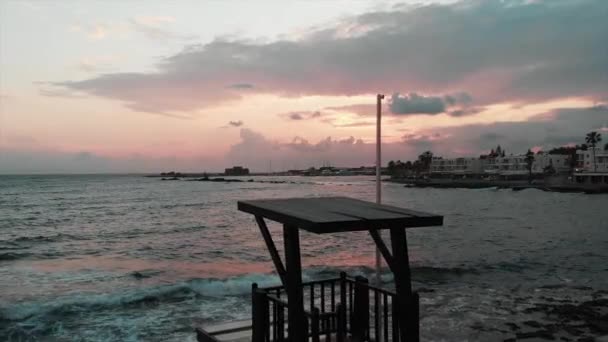 Luftaufnahme des Rettungsturms bei Sonnenuntergang mit Meereswellen und Stadthafen im Hintergrund — Stockvideo