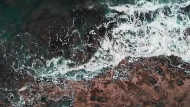 暴风雨海洋冲击岩石海滩的鸟瞰图。特写无人机拍摄海浪产生泡沫，在悬崖上飞溅 — 图库视频影像