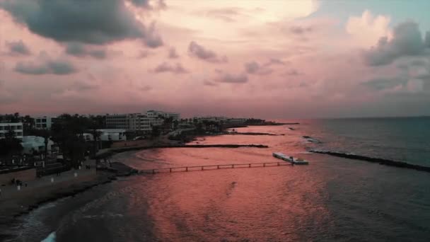 Vista aérea de un hermoso muelle con olas de mar golpeando la playa rocosa al atardecer — Vídeos de Stock