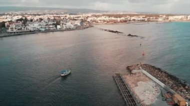 Gün batımında turistik bölgeden açık okyanusa yelken küçük bir beyaz balıkçı teknesi ile liman inşaatı Drone görünümü