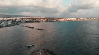 Beyaz balıkçı teknesi gün batımında küçük şehir körfezinden yola çıkıyor. İnsansız hava aracı görüntüsü