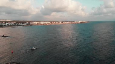 Küçük beyaz balıkçı teknesi arka planda mavi gökyüzü ve beyaz binalar ile açık okyanusa yelken. Havadan insansız hava aracı vuruldu