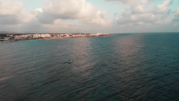 Bateau de pêche blanc navigue hors de la grande ville de villégiature dans la mer sereine sans vagues lors d'une journée ensoleillée. Vue aérienne du drone — Video