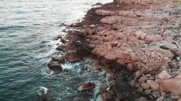 Drone vuela a lo largo de la orilla del mar con la playa rocosa. Vista aérea de grandes olas golpeando piedras del océano — Vídeo de stock