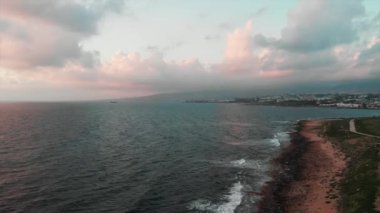 Gün batımında kayalık deniz kıyısı ve turistik yaya rıhtımı ile sınırsız okyanus boyunca uçan drone