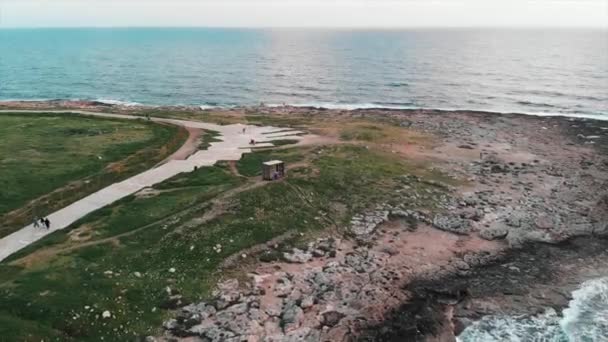 Vzdušný pohled na skalnaté pobřeží se zelenými trávníky a pěšinu pro pěší s pěší turistou. — Stock video
