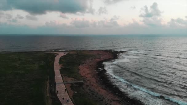 Aerial view of green tourist promenade with rocky beach. Drone shot of people walking along pedestrian path at beautiful sunset — Stock Video