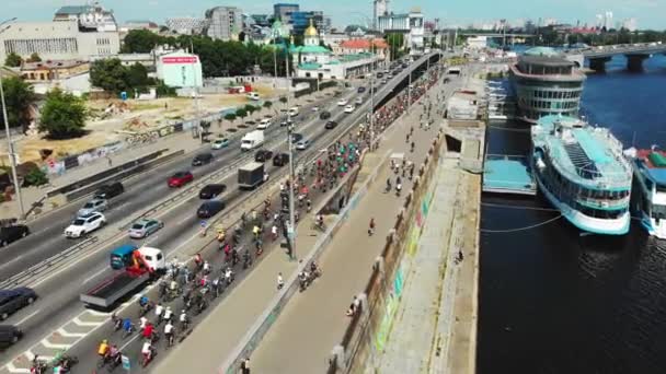 Colonne de jeunes cyclistes heureux conduisent le long de la route avec des voitures lors d'une journée chaude ensoleillée d'été. Drone shot — Video