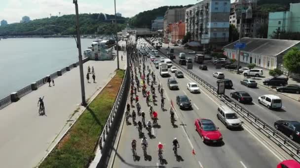 Tiro aéreo de dron del grupo de ciclistas en ropa deportiva brillante cabalgando lentamente por el centro de la ciudad a lo largo del muelle — Vídeo de stock