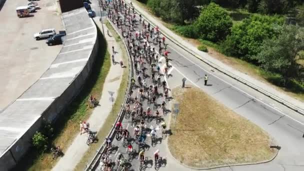 Vista aérea de los ciclistas en ropa deportiva brillante y cascos en bicicletas de montaña que viajan lentamente a través del verde parque de recreo turístico en el Día de la Bicicleta — Vídeos de Stock