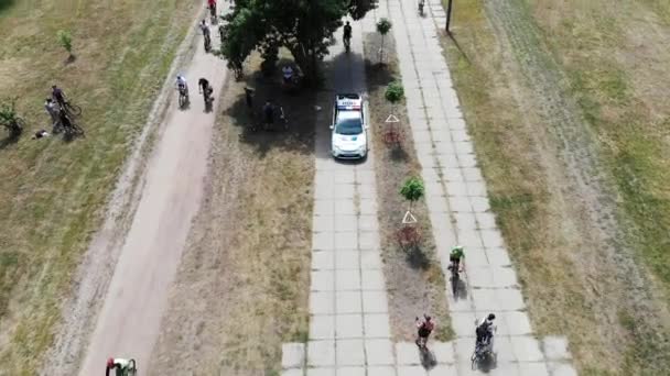 Politie auto rijdt op toeristische weg met een groep fietser in het groene stadspark — Stockvideo