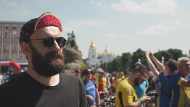 Kiev / Ucrania-junio, 1 2019 Retrato de un joven hipster guapo con barba en gafas de sol negras y gorra roja en el desfile de bicicletas. Movimiento lento — Vídeo de stock