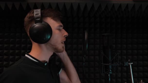 Pop male singer in headphones singing to professional microphone. Handsome boy is recording song. Slow motion — Stock Video
