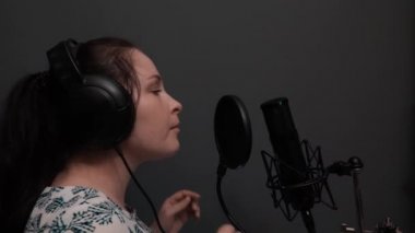 Kulaklık genç çekici pop kadın yıldız mikrofona şarkı. Sevimli kız kayıt stüdyosunda şarkı yapıyor. Müzik kaydı
