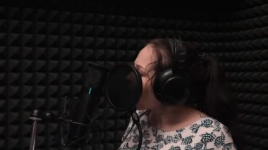 Genç kızın yakından yan görünümü düşüncesizce mikrofona şarkı söylüyor. Dramatik şarkı lar. Profesyonel kayıt provası