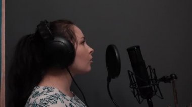 Genç romantik pop kadın şarkıcı şarkı yapıyor. Kız gri duvarlar ile ev profesyonel kayıt stüdyosunda şarkı. Profesyonel vokal müzik stüdyosu