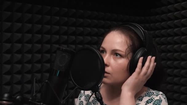Wanita muda romantis dengan headphone merekam lagu di studio vokal rumah. Gadis manis dengan rambut hitam panjang menyanyikan lagu — Stok Video