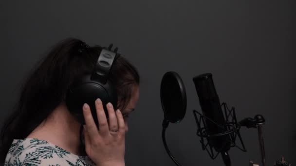 Mladá atraktivní dívka s dlouhými tmavými vlasy poslouchá hudbu ve sluchátkách. Portrét kavkazské ženy naslouchá Nahrávám. Vokální zkouška — Stock video