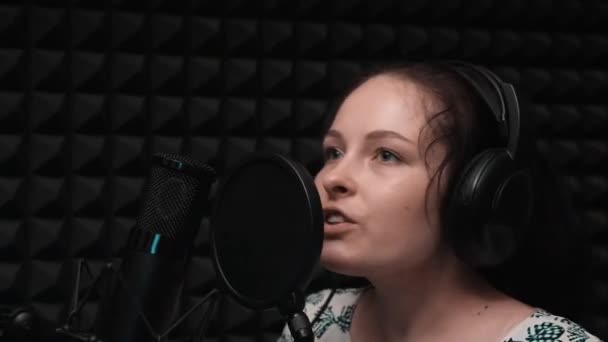 Canto emocional. Mulher caucasiana bonita cantando em estúdio de gravação. Estúdio de música vocal com microfone e fundo preto. Menina ensaiando na base de música — Vídeo de Stock