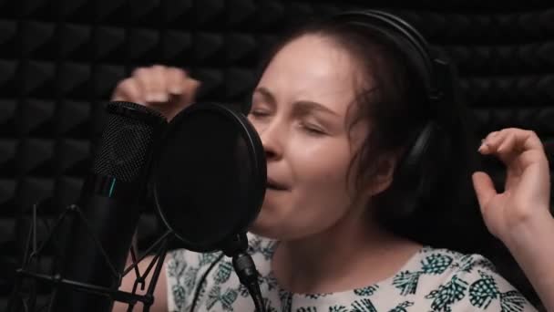 Mädchen singt emotional im Vokalstudio. attraktives Mädchen nimmt Gesangsunterricht. Aufnahme von Songs im Studio. Großaufnahme von jungen niedlichen kaukasischen Mädchen mit Kopfhörern singt zum Mikrofon. Gefühlvoller Gesang — Stockvideo